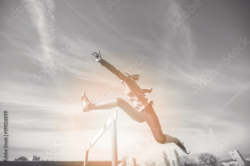 Foto Female athlete jumping above the hurdle during the race