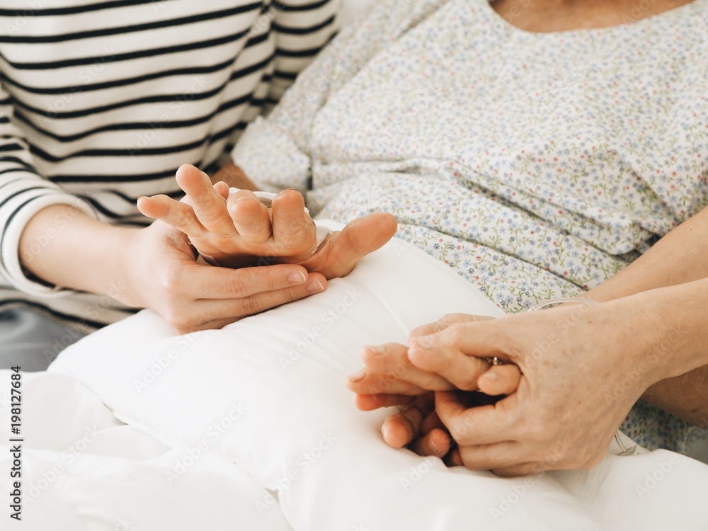 Fototapeta close up daughter hands holding grandmother hand in bedroom.