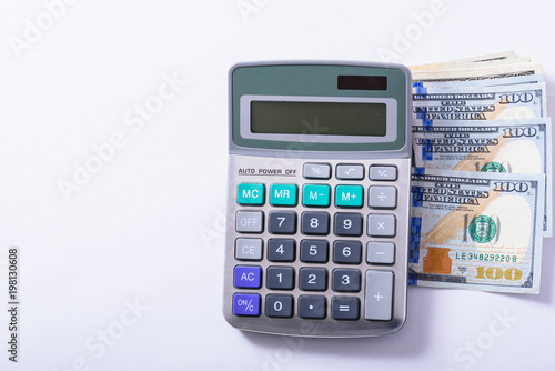 A calculator on top of some American money on a white background with negative space for text