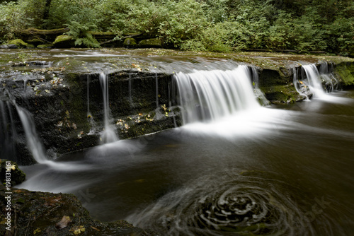 Fototapeta Naklejka Na Ścianę i Meble -  Flowing creek over a low waterdall into a dark swirling pool