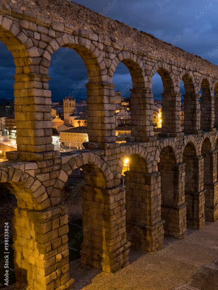 Nightly Segovia, Spain at the ancient Roman aqueduct. The Aqueduct of Segovia, located in Plaza del Azoguejo, is the defining historical feature of the city.