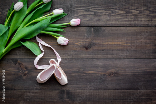 Ballet shoes near delicate flowers on dark wooden background top view copy space