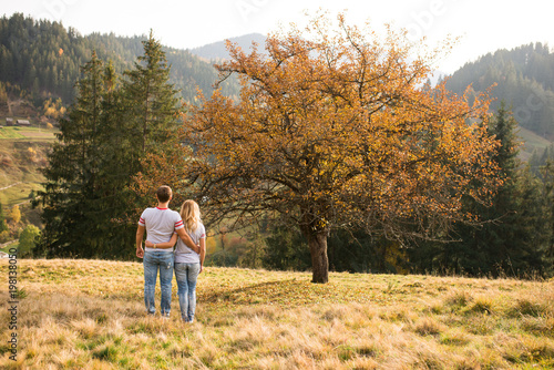 Happy girl and boy holding around each other and walking in nature at autumn. The girl and boy in grey T-shirts and jeans, tenderly embracing each other. 