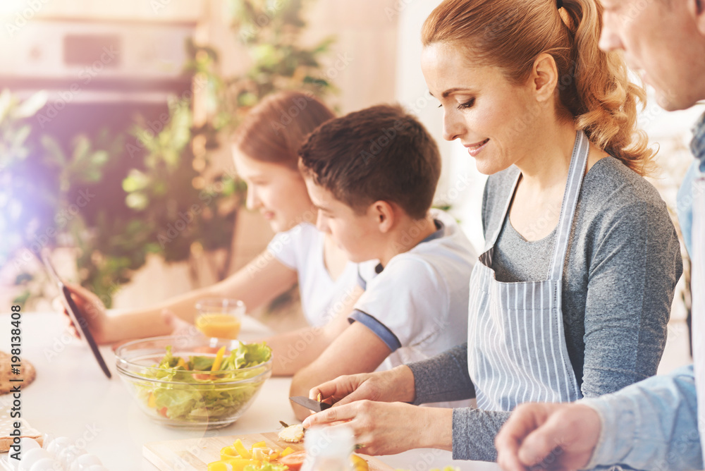 Be attentive. Delighted mother bowing head while looking attentively at vegetables while preparing dinner Be attentive. Delighted mother bowing head while looking attentively at vegetables while preparing dinner