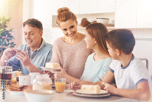 Express positivity. Delighted blonde woman standing between her daughter and husband  keeping smile on her face while talking to children