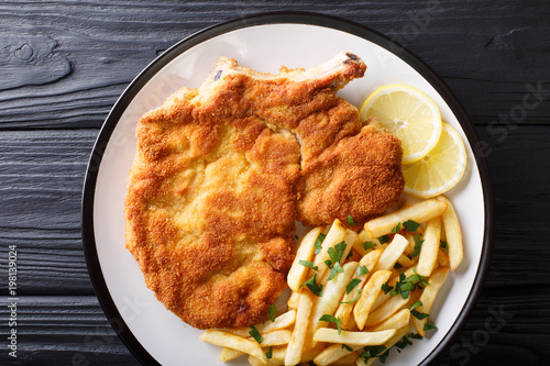 Fried veal cutlet Milanese with lemon and French fries close-up. horizontal top view