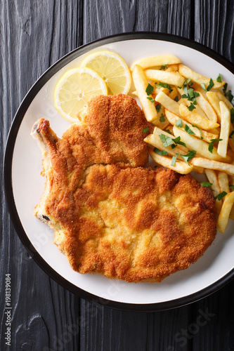 Fried veal cutlet Milanese with lemon and French fries close-up. Vertical top view