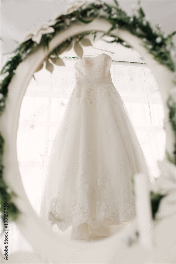 the wedding dress hangs on a hanger and is reflected in the mirror, the bride's morning the wedding dress hangs on a hanger and is reflected in the mirror, the bride's morning