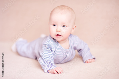 Pretty baby girl crawling in bed over beige background. Childhood.