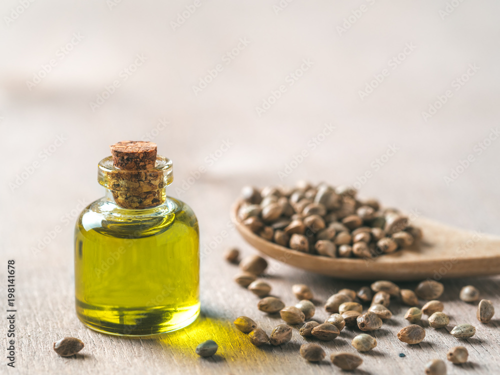 Hemp seeds and hemp oil on brown wooden table. Hemp seeds in wooden spoon and hemp essential oil in small glass bottle. Copy space for text Hemp seeds and hemp oil on brown wooden table. Hemp seeds in wooden spoon and hemp essential oil in small glass bottle. Copy space for text