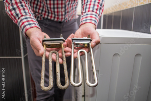 the repairman keeps a working new heating element and a faulty dirty teng close-up from the washing machine photo