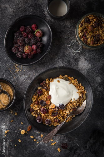 homemade granola (hazelnuts, raisin, dried cranberry, pumpkin, sesame and sunflower seeds) with yogurt in black bowl