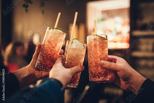 Three male hands holding three cocktail glasses againt blurred background in a c Fototapet