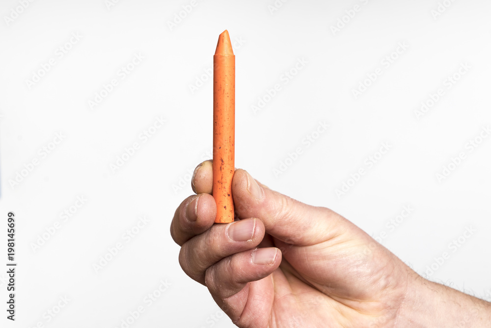 An orange wax crayon in the hand An orange wax crayon in the hand
