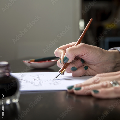 Woman make calligraphy writings, make art on a paper using pen brush and sign pen. Adult, old hands of a calligrapher woman. Lifestyle image of a design process