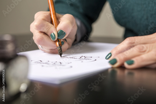 Woman make calligraphy writings, make art on a paper using pen brush and sign pen. Adult, old hands of a calligrapher woman. Lifestyle image of a design process photo