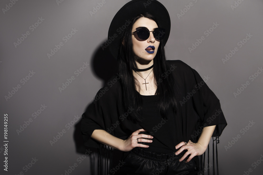 Gothic caucasian woman in dark dress on a grey neutral background. Contrast light. Sad, thoughtful emotions Gothic caucasian woman in dark dress on a grey neutral background. Contrast light. Sad, thoughtful emotions