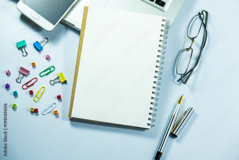 Top view of laptop, blank notebook, paper clips and smart phone with white background and copy space. Top view of laptop, blank notebook, paper clips and smart phone with white background and copy space.