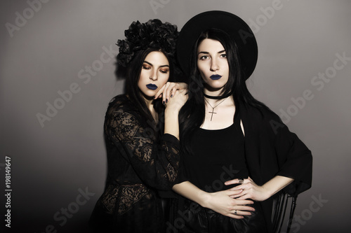 Gothic caucasian women in dark dresses on a grey neutral background. Contrast light. Sad, thoughtful emotions