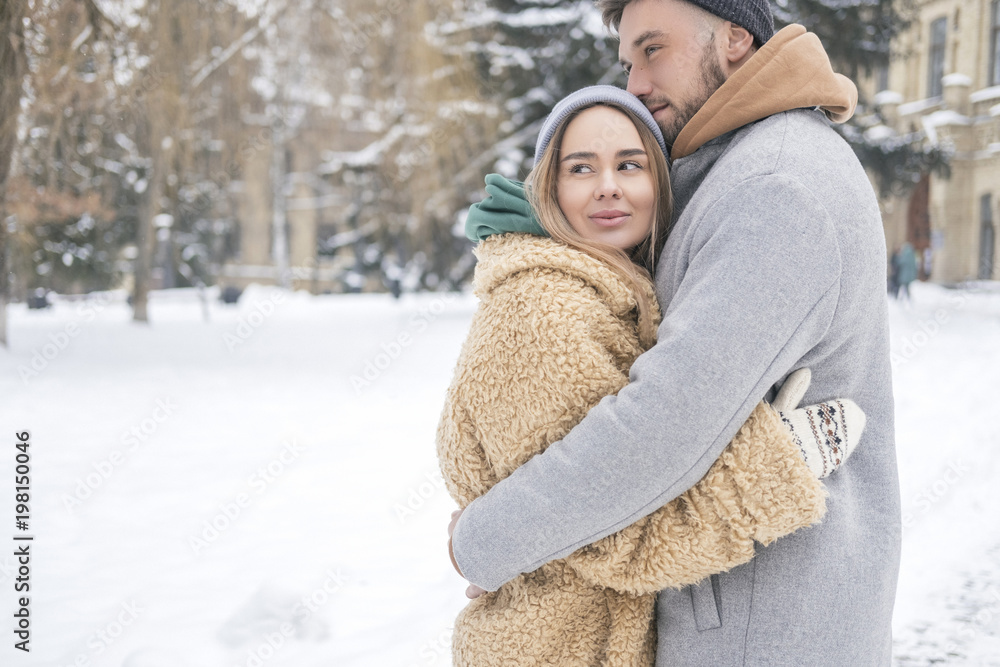 Stylish caucasian couple of man and woman waling in the european city park in winter. Cold, snowy day. Space for text