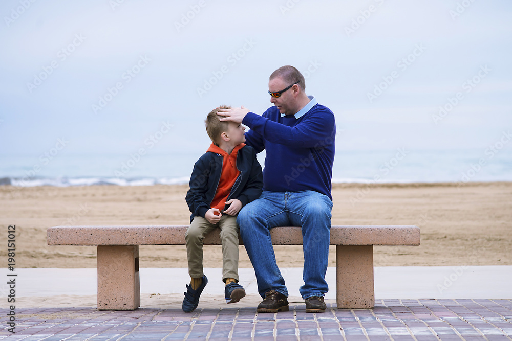 boy with father talking on a bench by the sea in spring boy with father talking on a bench by the sea in spring