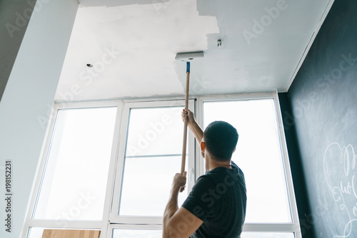 the man paints the walls and the ceiling in gray color, standing with his back to the camera. Focus on the roller. Painting and repair of the room.