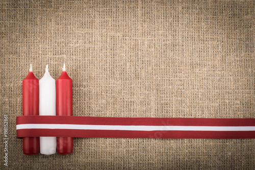 Fotografi Composition of three red white candles and latvian flag ribbon