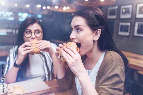 Best meal. Attractive delighted nice woman holding a burger and eating it while being hungry
