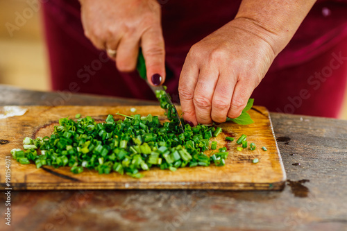 female hands cut green young onion on wooden board