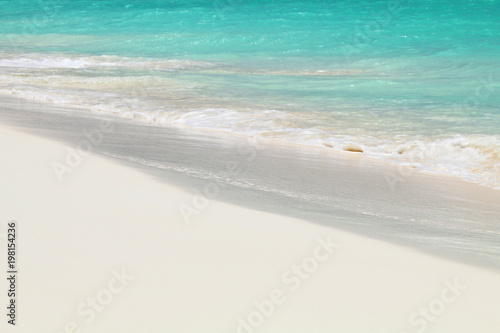 A small wave of ocean foams on the sandy Caribbean beach.