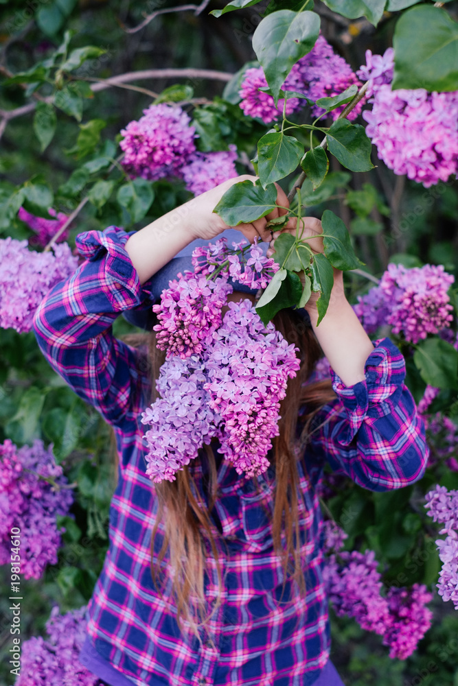 Photo of young model girl in colorful shirt hiding her face in violet lilac Photo of young model girl in colorful shirt hiding her face in violet lilac