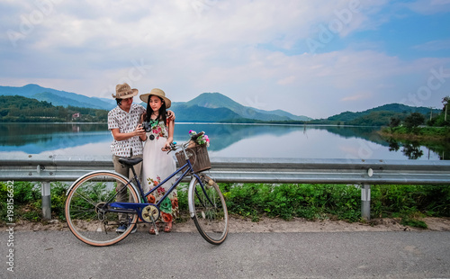couple traveler standing beside bicycle near the lake background is mountain on vacation.Asia tourists have romance time and enjoying for holiday.