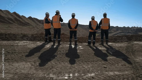 Panorama shot of a group of workers in overalls actively speaking on board a bauxite quarry.
