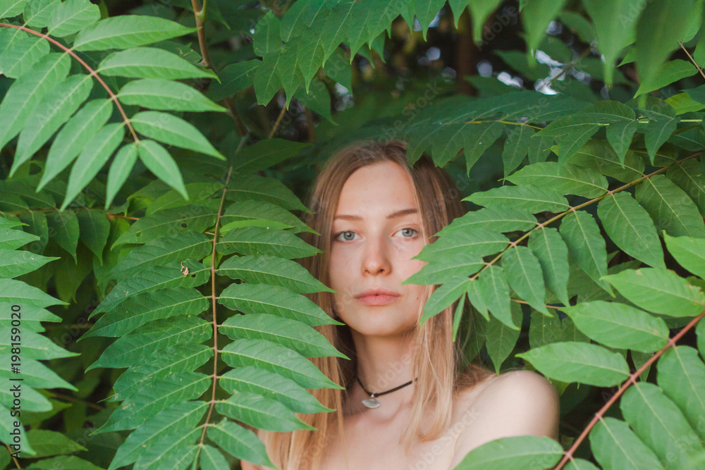 Portrait of beautiful young woman in green leaves, blonde pretty lady in spring bushes Portrait of beautiful young woman in green leaves, blonde pretty lady in spring bushes