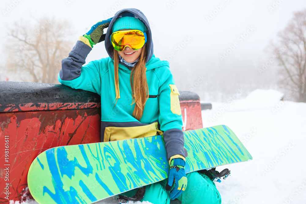 Beautiful happy young snowboarder sitting with her snowboard.