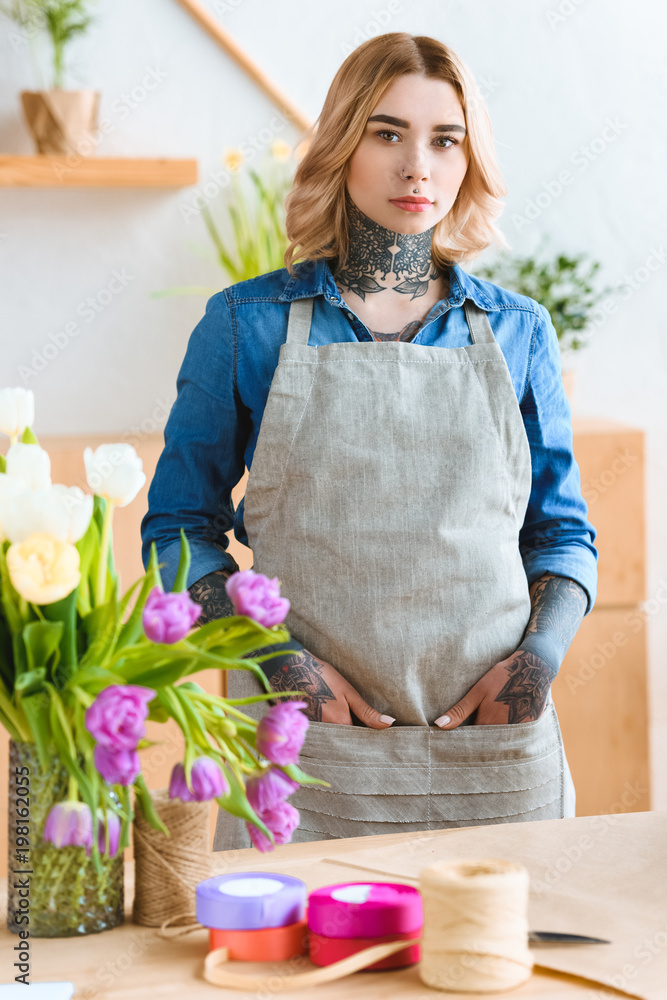beautiful young florist in apron looking at camera in flower shop beautiful young florist in apron looking at camera in flower shop