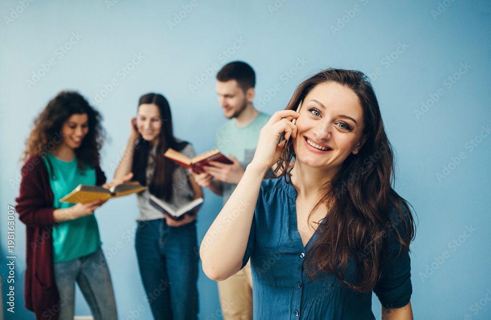 Female student with mobile phone,talk and smile. Group of happy college students standing together in the hallway behind. Female student with mobile phone,talk and smile. Group of happy college students standing together in the hallway behind.