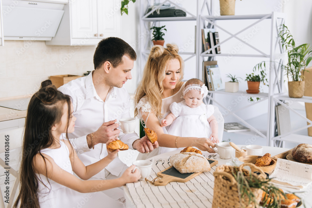 Parents and their two children eating and drinking tea at kitchen table, happy family Parents and their two children eating and drinking tea at kitchen table, happy family