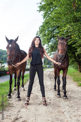 Pretty young woman walking two horses