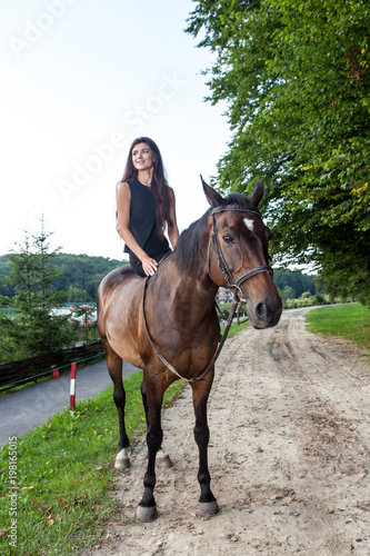 Pretty young woman riding a brown horse © alexandco