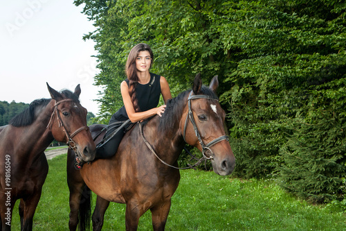 Pretty young woman riding a brown horse © alexandco