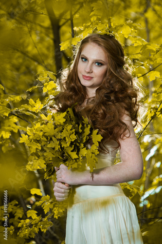 Red haired girl in autumn forest. Beautiful girl in autumn forest. Beautiful elegant red hair girl standing in a park in autumn. Outdoors portrait of beautiful girl with red hair and blue eyes