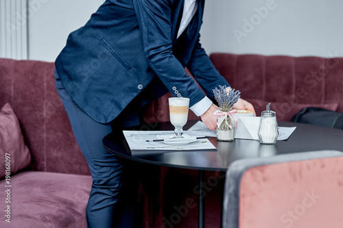 A business man in a suit, spreads out papers on a table, drinks coffee in a cafe