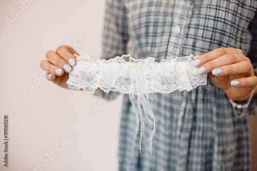 Young woman is holding a white lace wedding garter of bride.