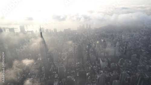 New York City sunrise aerial view flying south over Midtown Manhattan, facing the East River, with low level clouds.
