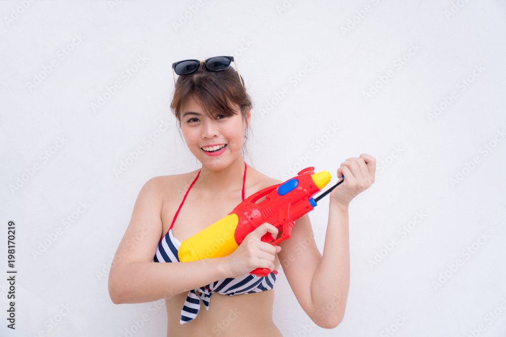 Beautiful girl in bikini two piece. She holds a red-yellow water gun. She prepared to go out to play the Songkran Festival. Concepcion Songkran Festival. White background. Beautiful girl in bikini two piece. She holds a red-yellow water gun. She prepared to go out to play the Songkran Festival. Concepcion Songkran Festival. White background.