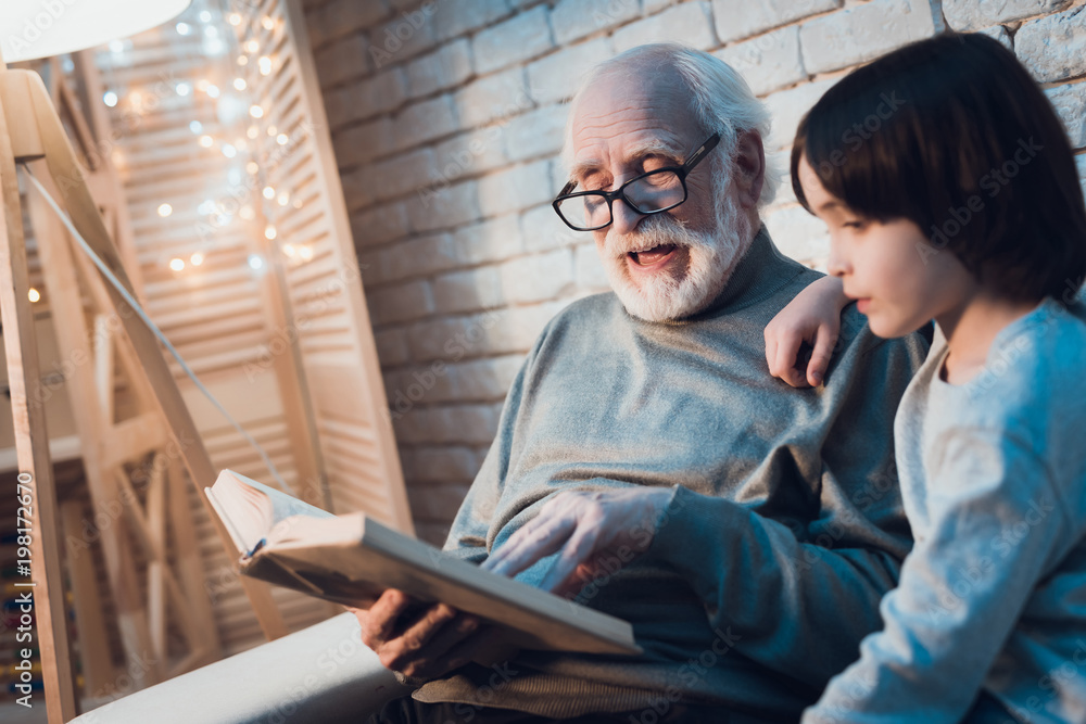 Grandfather and grandson at night at home. Granddad is reading fairy tales book. Grandfather and grandson at night at home. Granddad is reading fairy tales book.