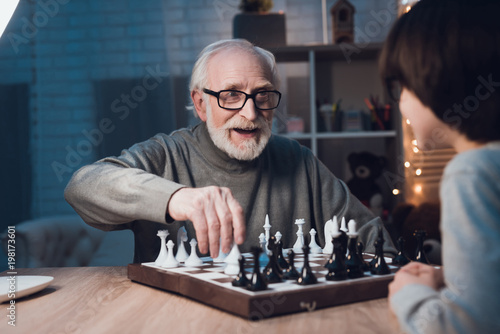 Grandfather and grandson are playing chess together at night at home. photo