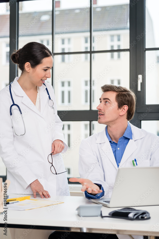 Young female physician using a tablet PC while asking for advice from her experienced male colleague in the office a modern hospital Young female physician using a tablet PC while asking for advice from her experienced male colleague in the office a modern hospital