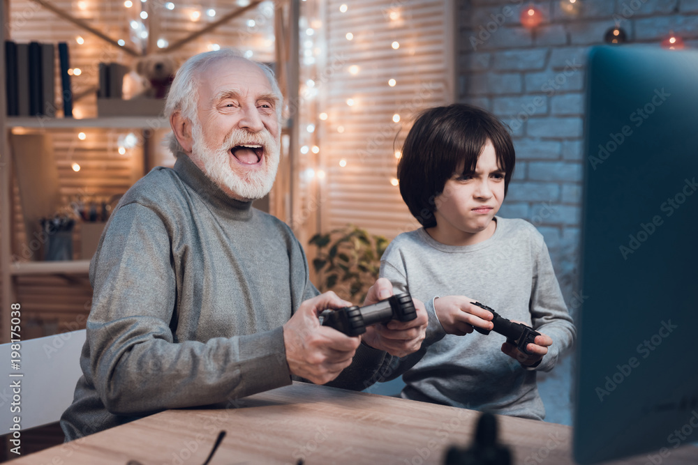 Grandfather and grandson are playing video games on computer at night at home. Grandfather and grandson are playing video games on computer at night at home.
